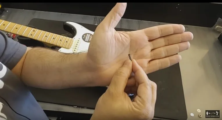 Close up view of a hand adjusting the metal tremolo tension springs inside the back cavity of a Fender Stratocaster guitar