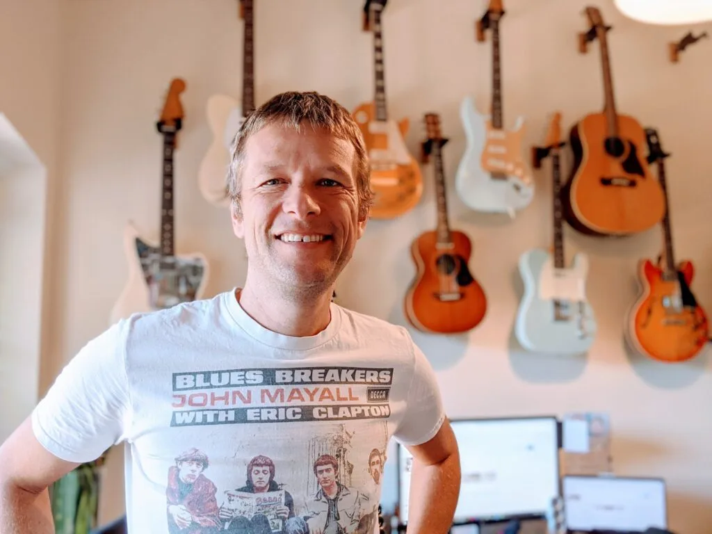 Guitar teacher Simon Morel standing with guitar wall in his music studio space