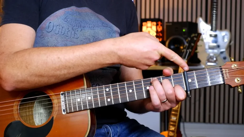Simon Morel demonstrating proper guitar capo placement on an acoustic guitar fretboard from the bass side.