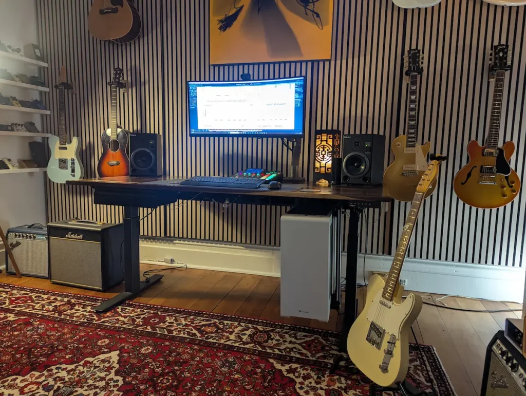 Home guitar practice rig showing a tube amp, UA OX Amp Top Box, Rodecaster Pro 2, and Roland monitors set up on a sit-stand desk