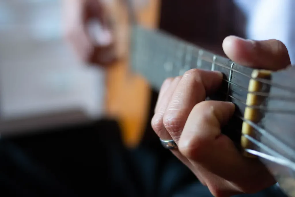Close-up of fingertips pressing down on steel acoustic guitar strings on a fretboard