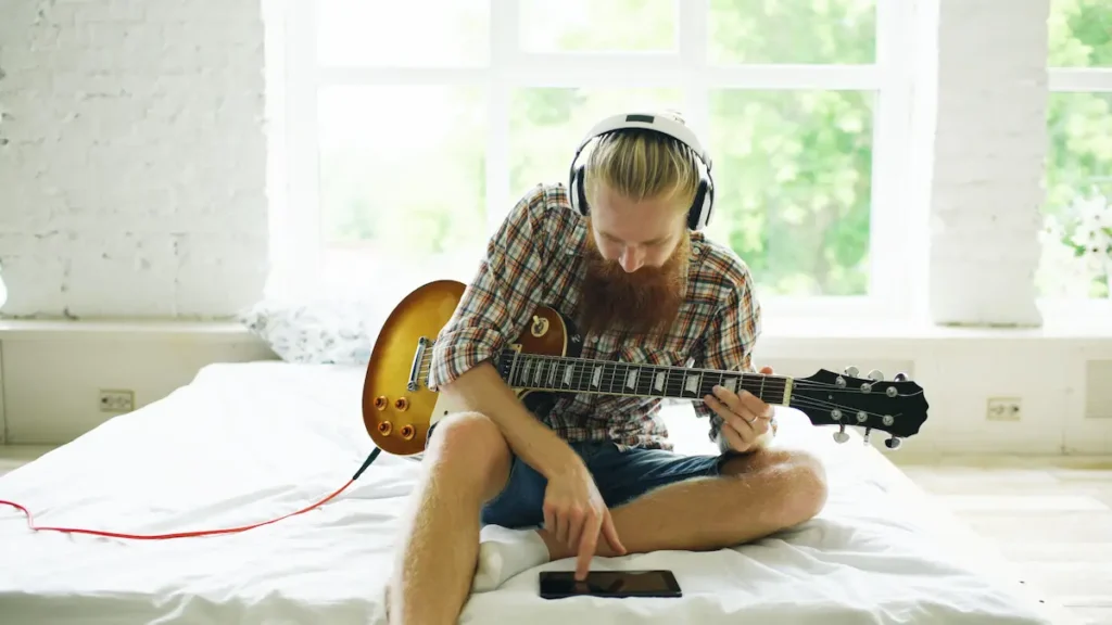 Person listening to music through headphones while finding chords on a guitar fretboard